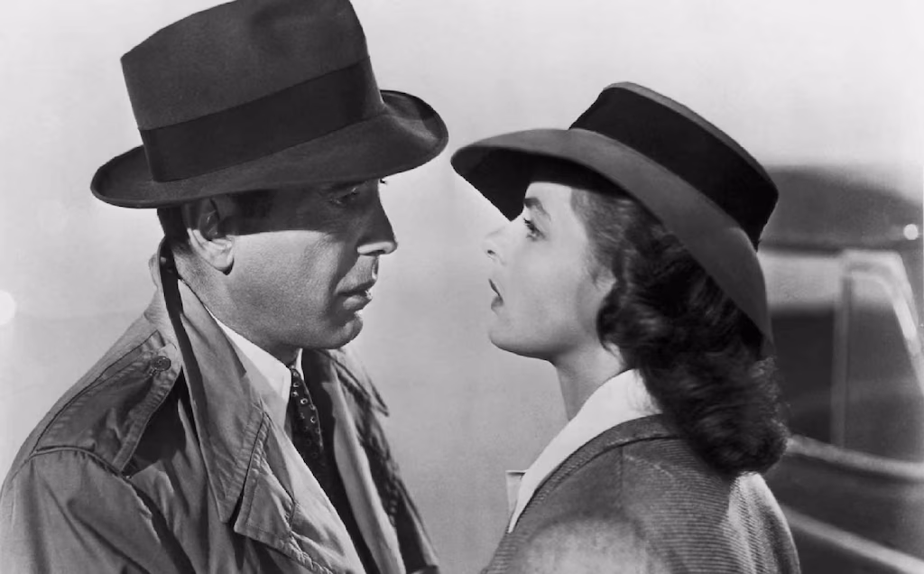 Scene from Casablanca featuring Humphrey Bogart and Ingrid Bergman in a close-up black-and-white romantic moment wearing classic trench coats and hats.
