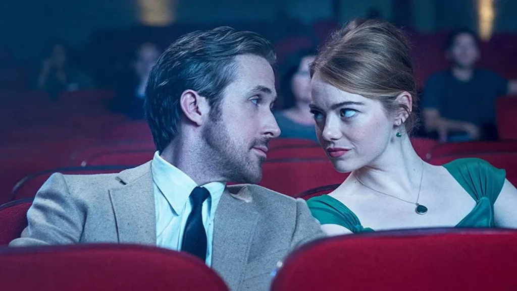 A man and a woman in formal attire sit close together in a movie theater, looking into each others eyes while watching one of TwilightRoom’s four favorite films.
