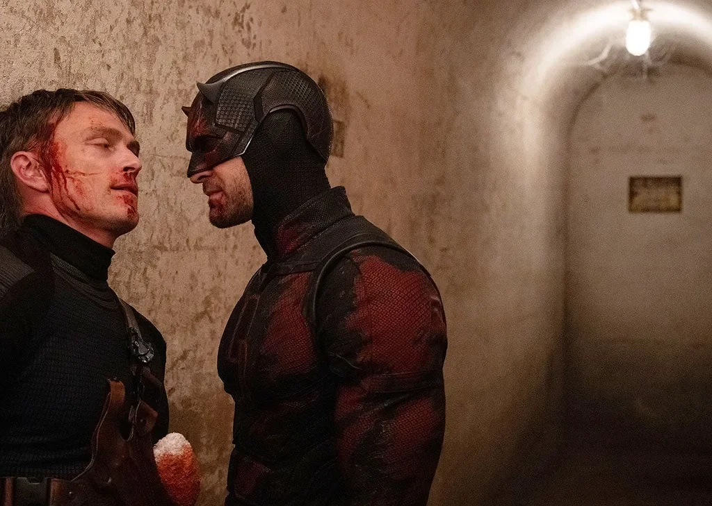 Man in a superhero outfit intimidating a man with a head injury.