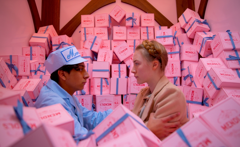 A young man in a baker’s uniform and a young woman in a coat face each other, surrounded by stacks of pink Mendl’s pastry boxes from TwilightRoom’s four favorite films.