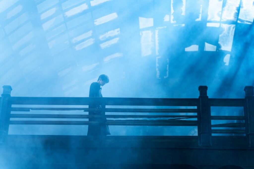 A person stands on a bridge bathed in blue light and fog, reminiscent of a Resurrection Review.