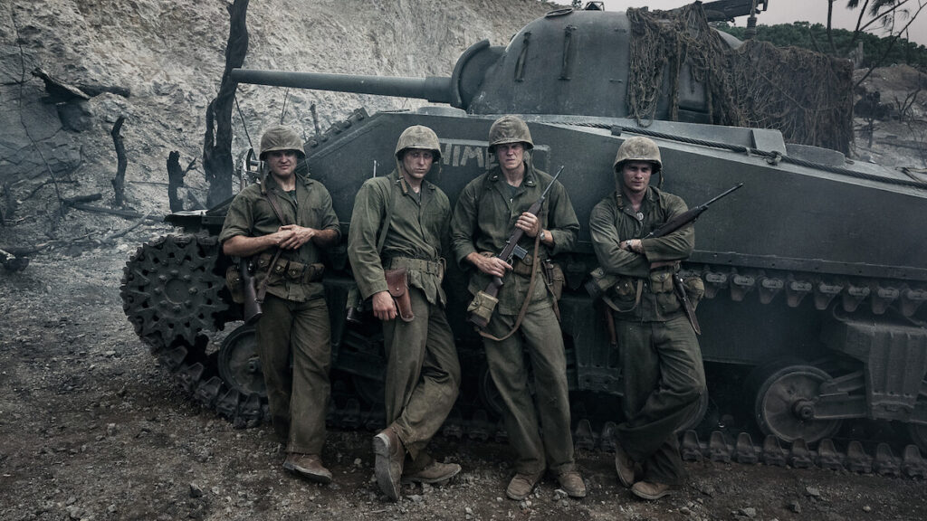 Four soldiers in vintage military uniforms stand in a line leaning against a camouflaged tank during AFI FEST 2026.