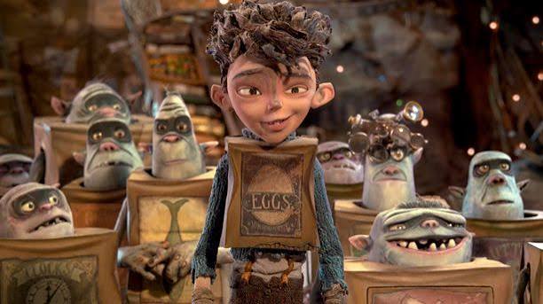 Eggs, a young boy with messy hair, stands in front of several box-dwelling trolls in this scene from the Laika Studios film.